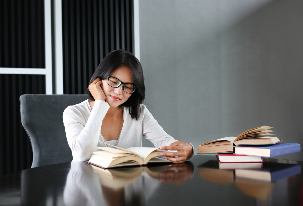 Asian woman in glasses reading books in a library