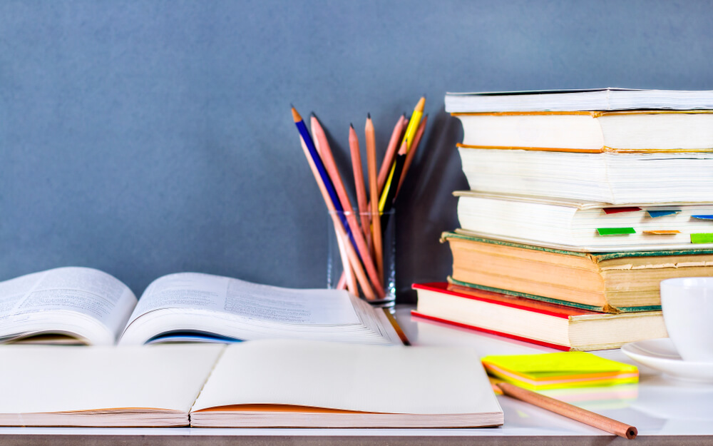 textbooks stacked near pencils on a table